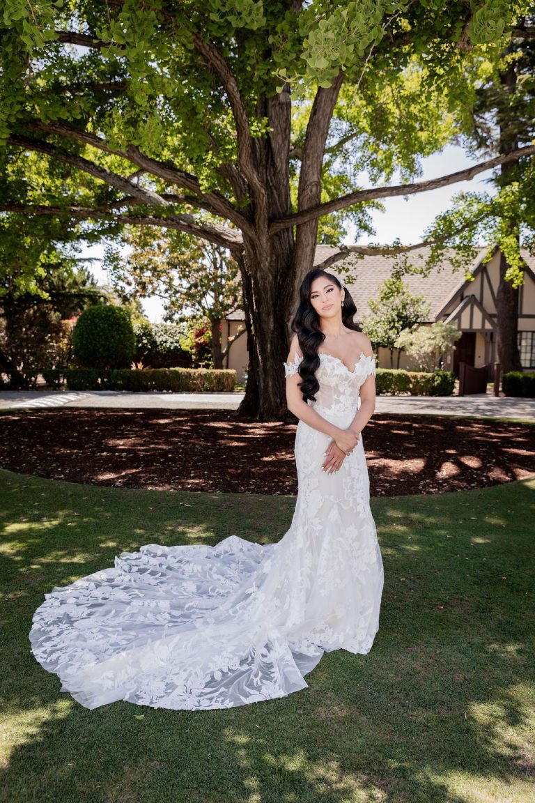 Bride standing solo on lawn holding gown train