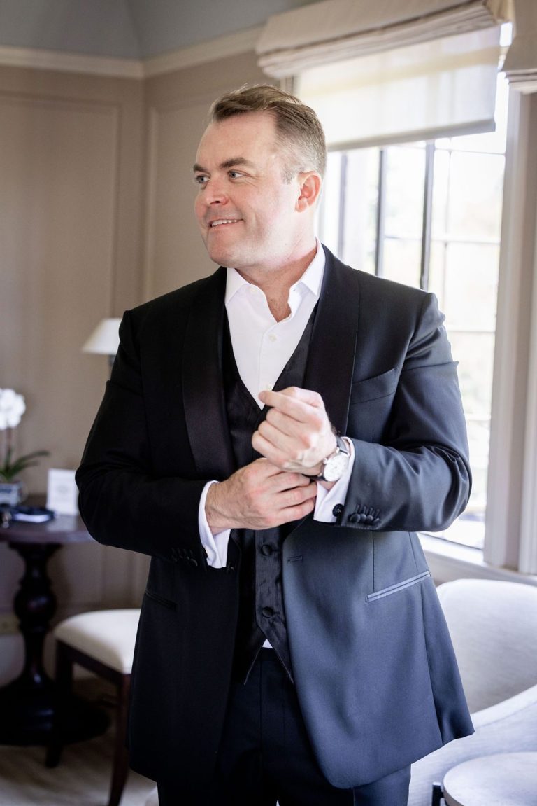 Groom fastening cufflink looking toward window