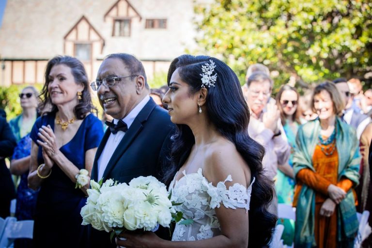 Emotional bride with bouquet processing between joyful clapping family