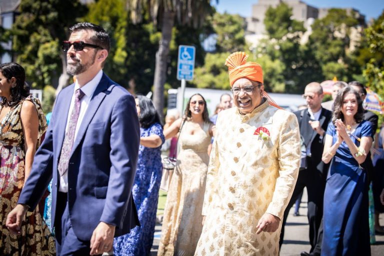 Father in cream sherwani walking in procession with guests clapping