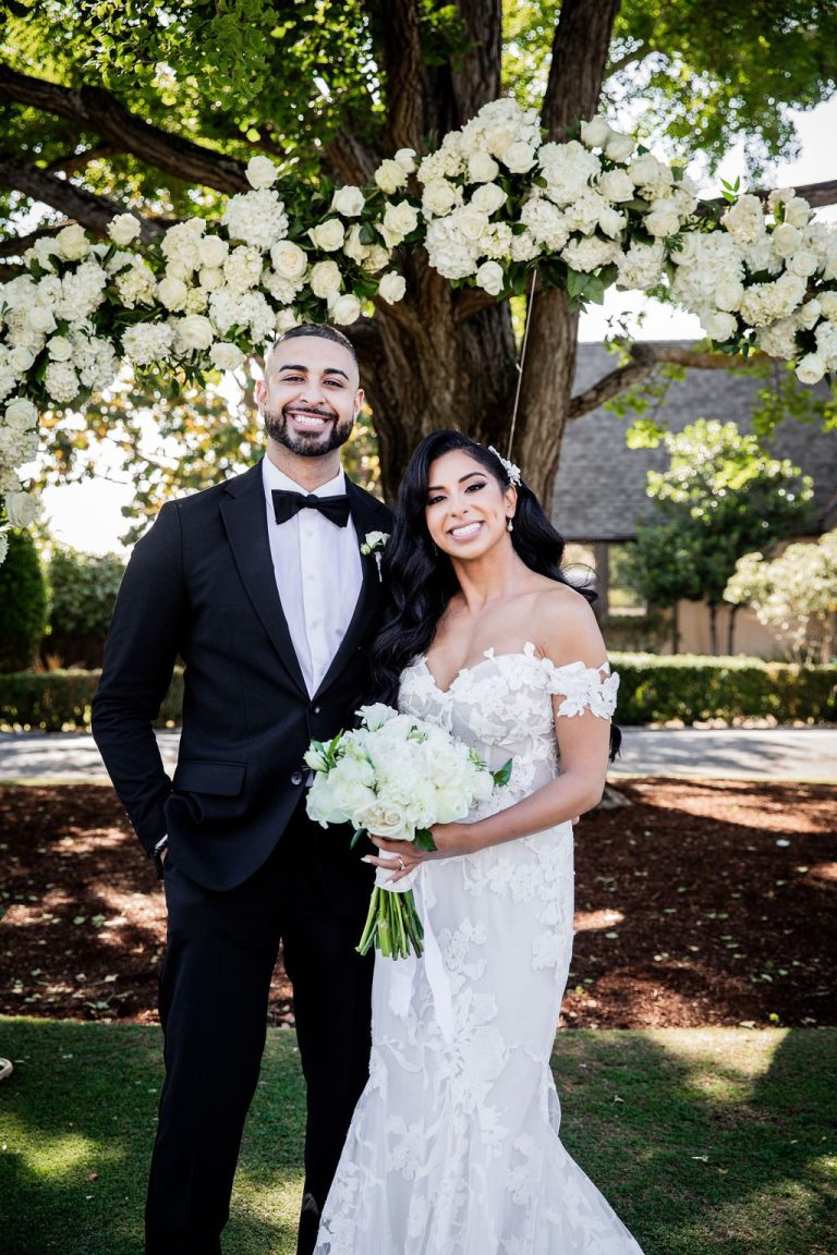 Groom and bride with bouquet pose at floral arch