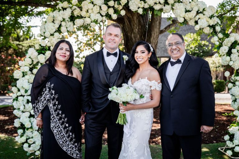 Bride with bouquet and family pose at floral arch