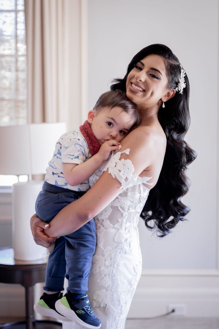 Bride beaming while holding young boy close indoors
