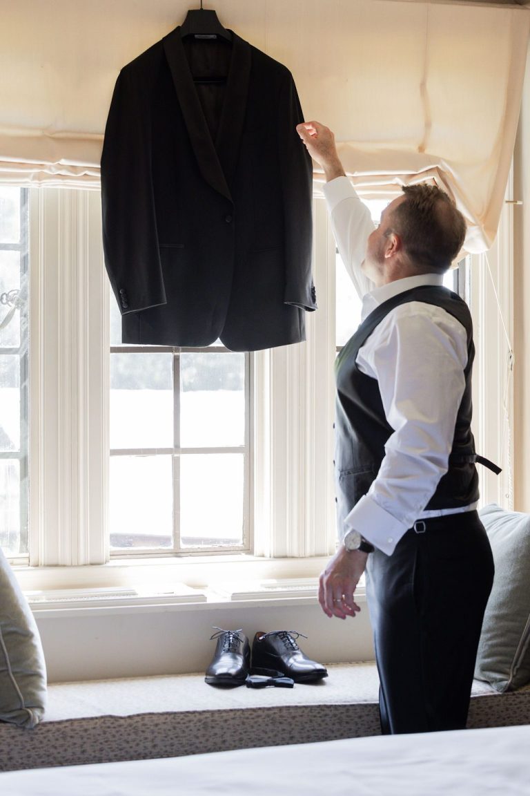 Groom reaching for suit jacket hanging in window