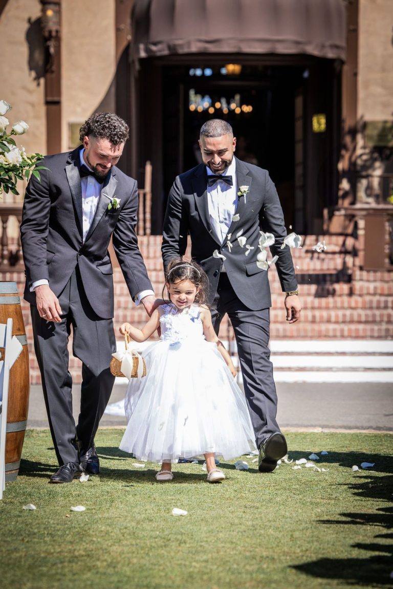 Groomsmen walking flower girl scattering petals down aisle