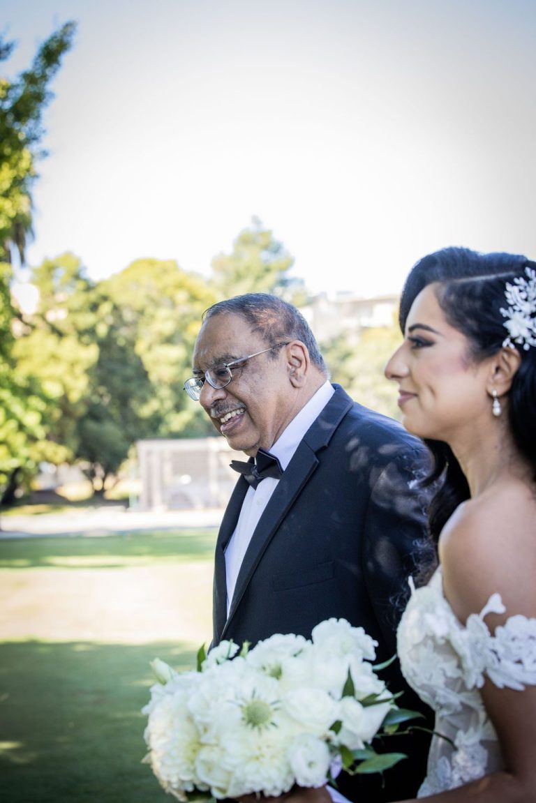 Bride smiling beside escort holding white bouquet outdoors