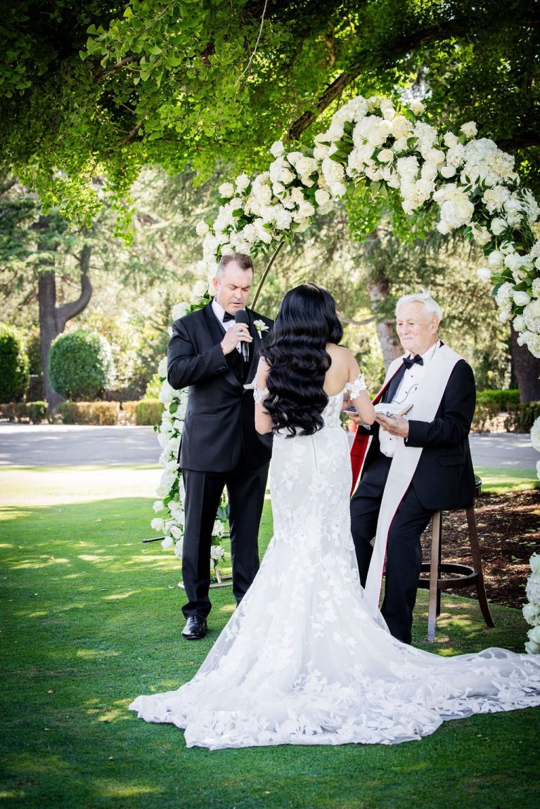 Bride and groom holding hands facing officiant on lawn