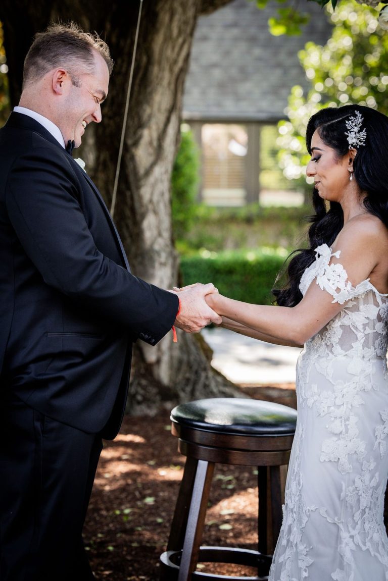 Groom holding bride hands beside candle table during vows