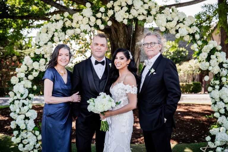 Bride with bouquet and three guests at floral arch