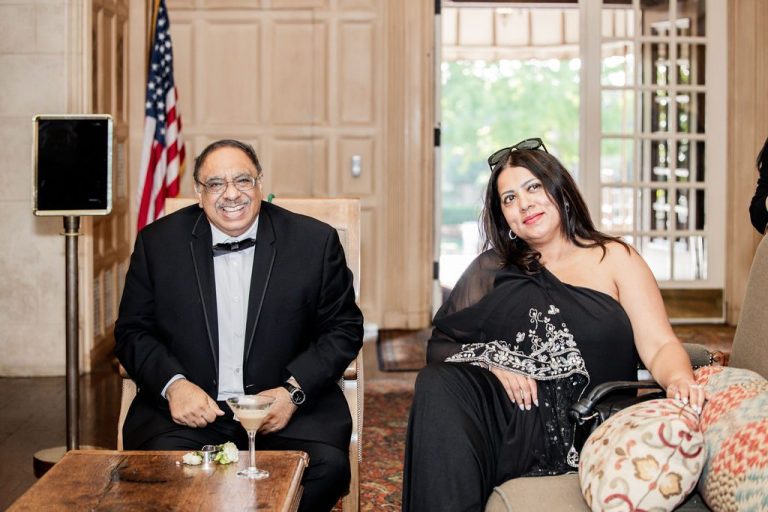 Two guests seated posing near flag indoors