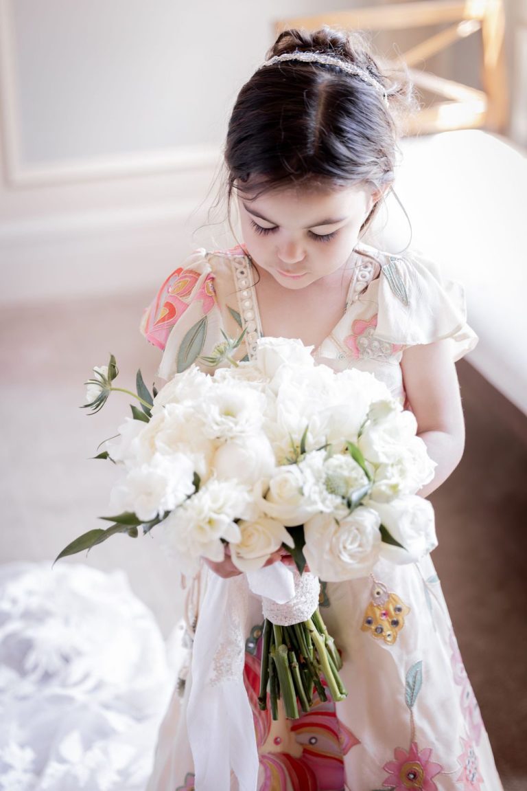 Flower girl in floral dress holding white bouquet