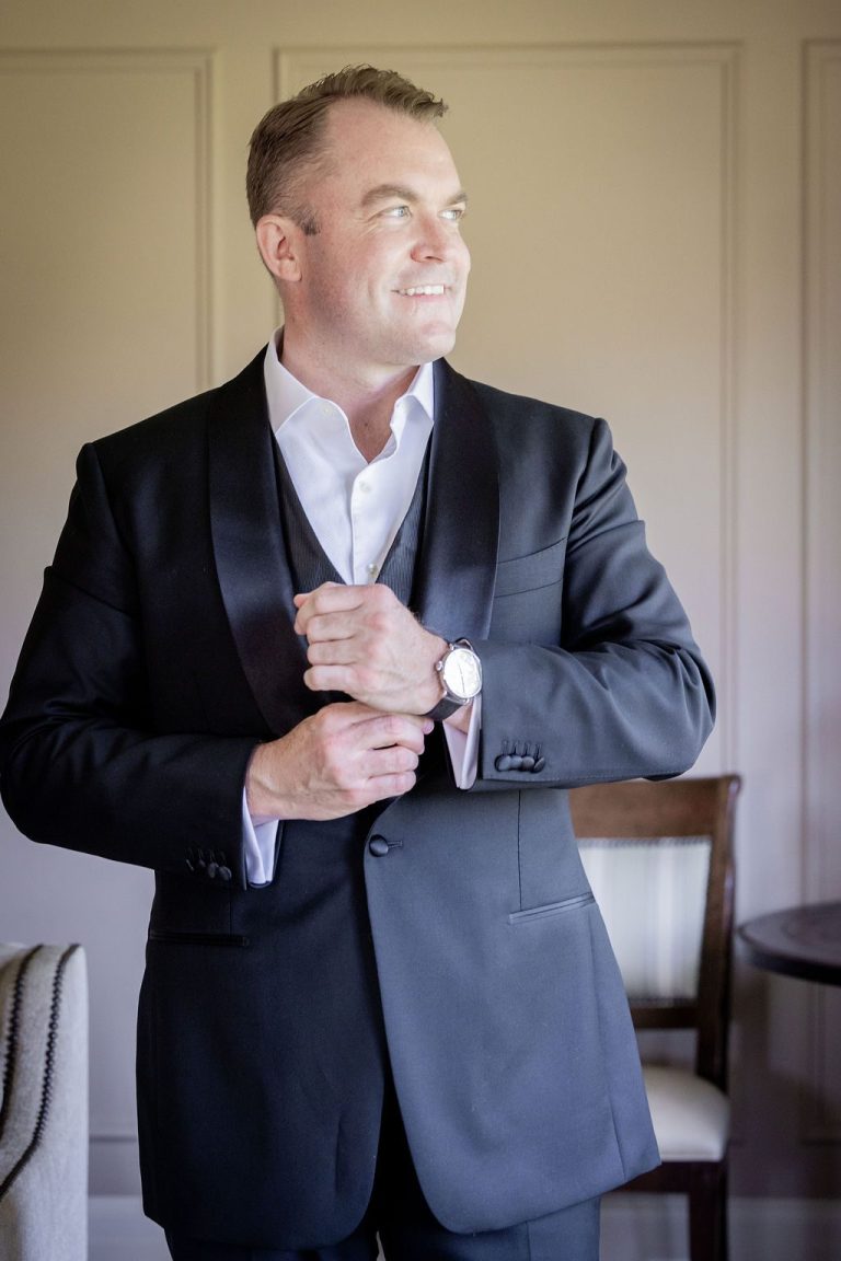 Groom adjusting cuff gazing toward window light