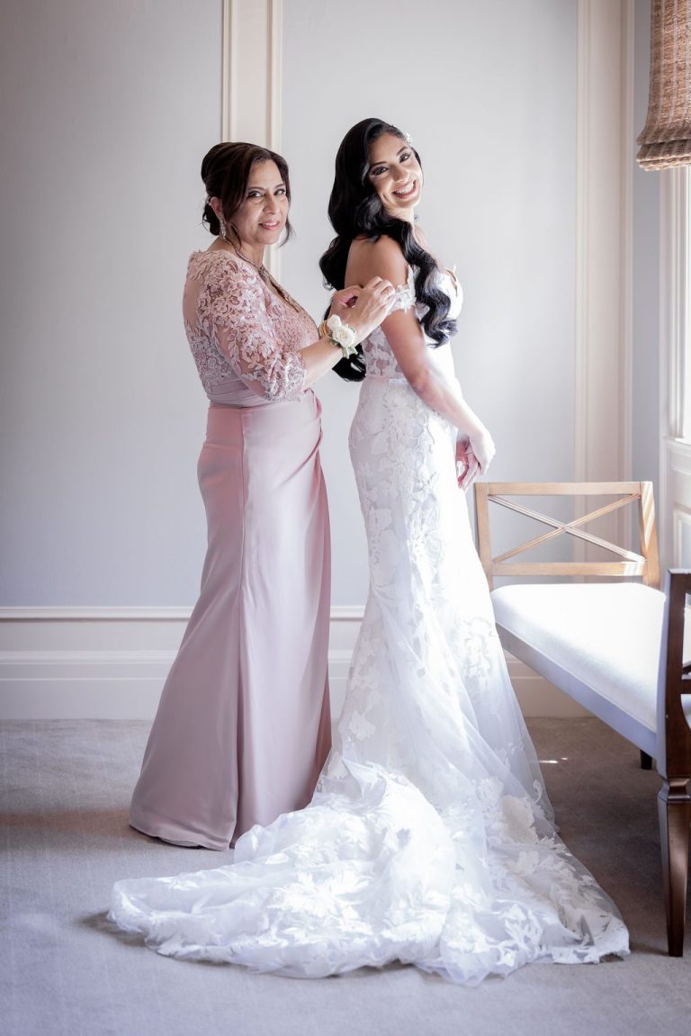 Bride embracing mother in pink dress by window