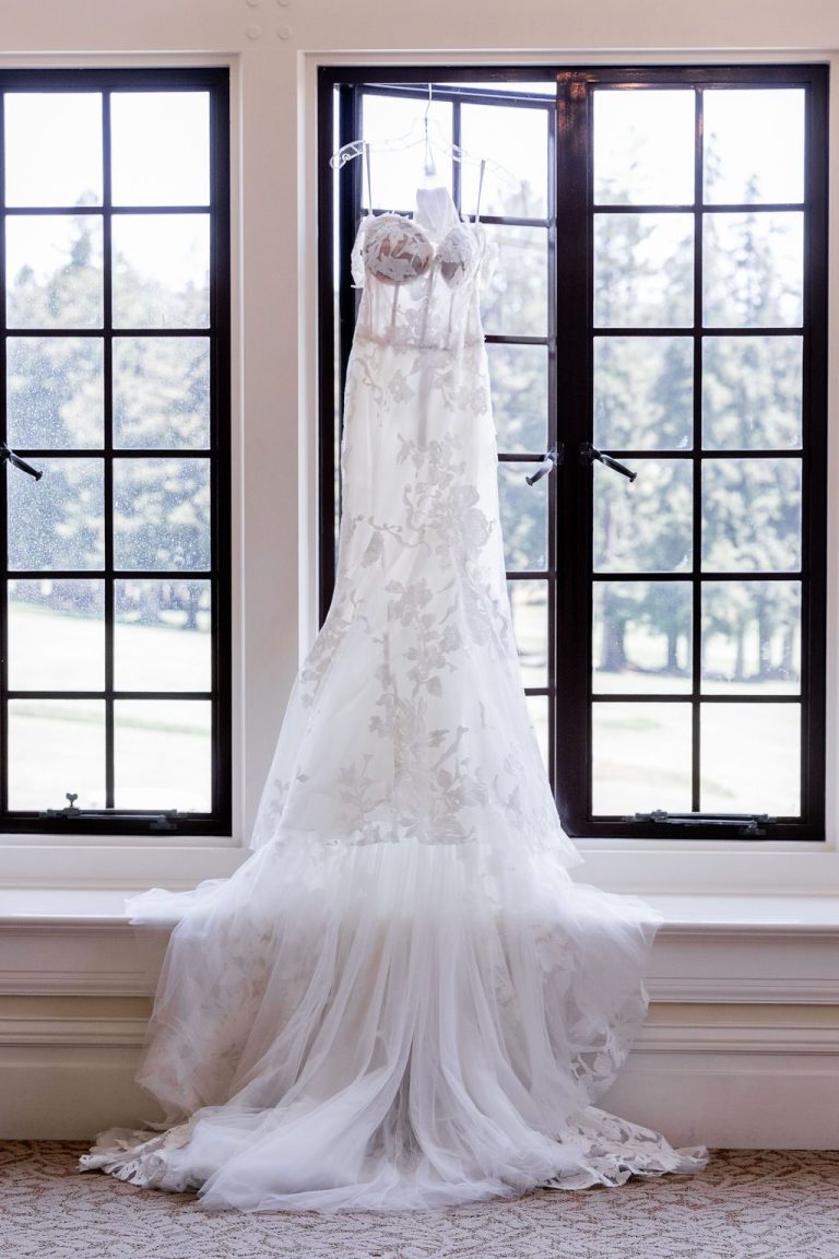 Detailed lace wedding gown hanging in bright window