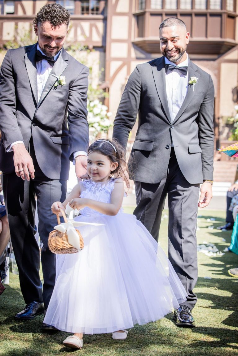 Two groomsmen walking flower girl down aisle