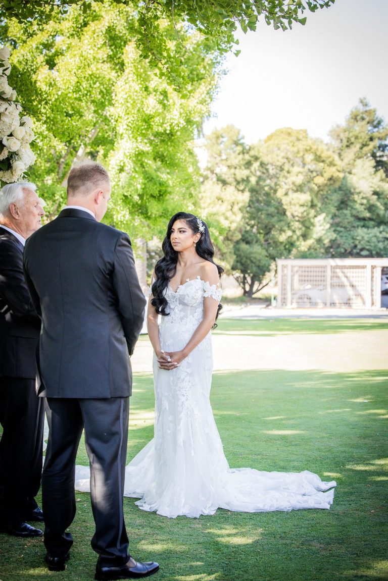 Bride and groom facing each other on sunlit lawn