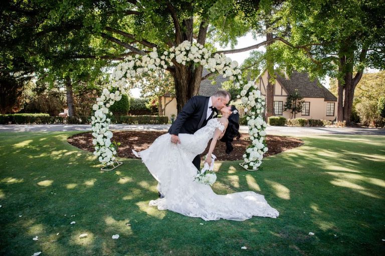 Groom dipping and kissing bride under floral arch