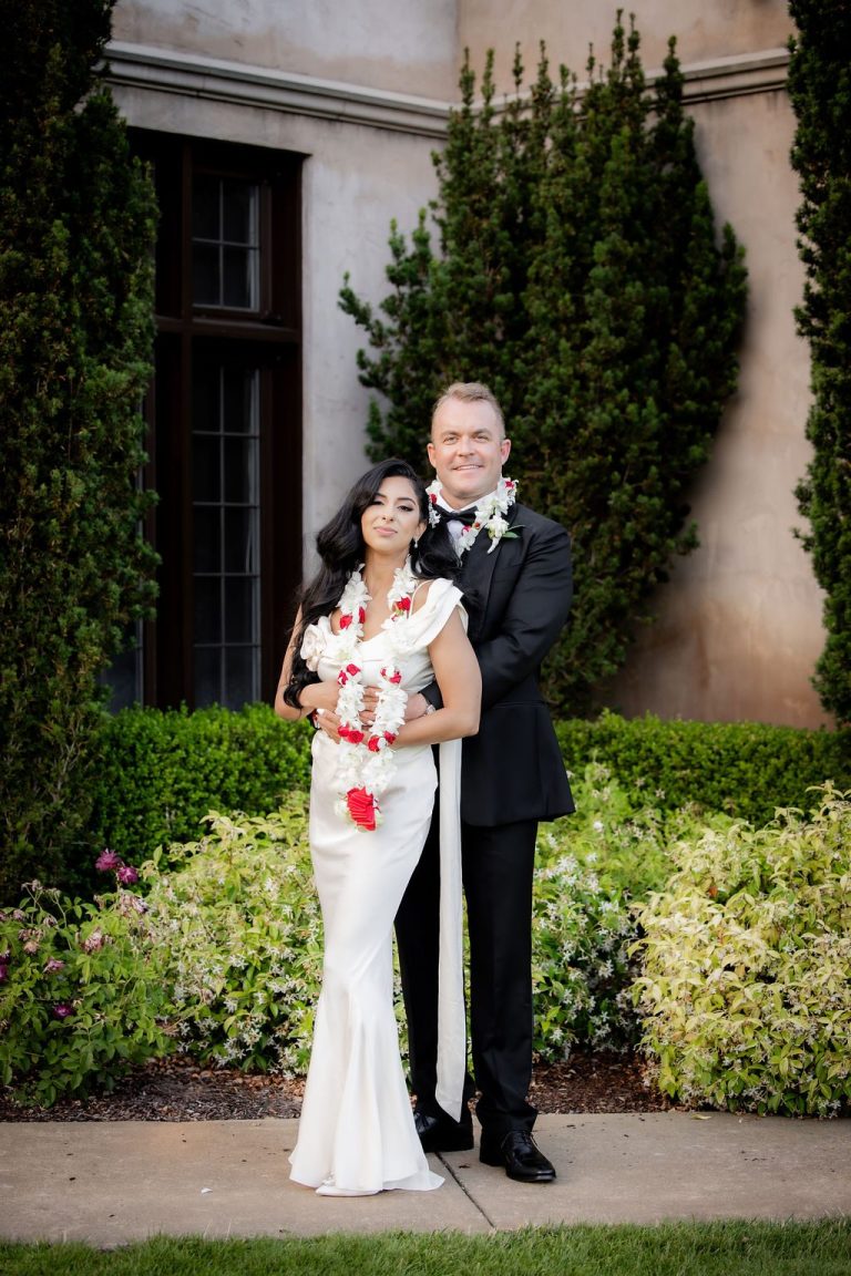 Bride and groom embracing among greenery, floral garland