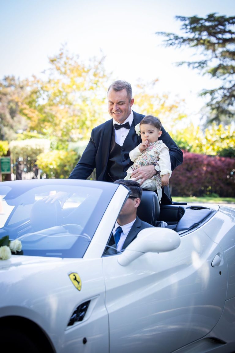 Man holding toddler in white sports car during procession