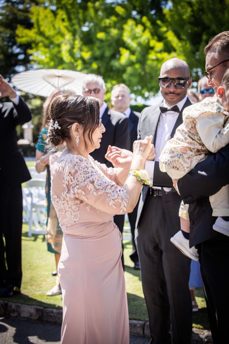 Woman greeting man holding child among tuxedoed guests