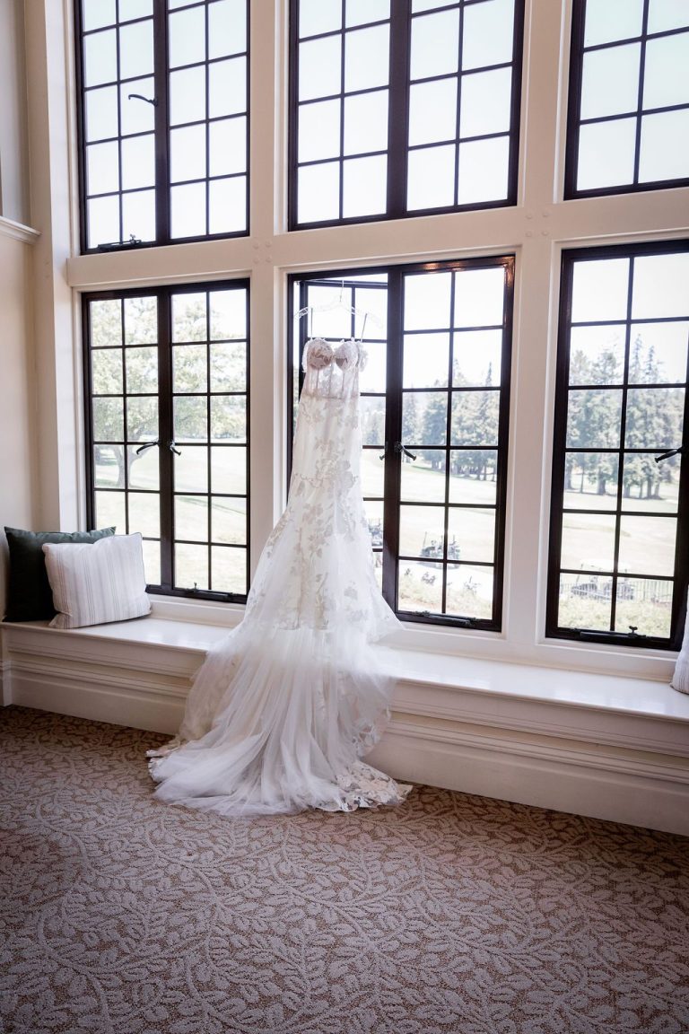 Wedding gown hanging in tall window with train pooling