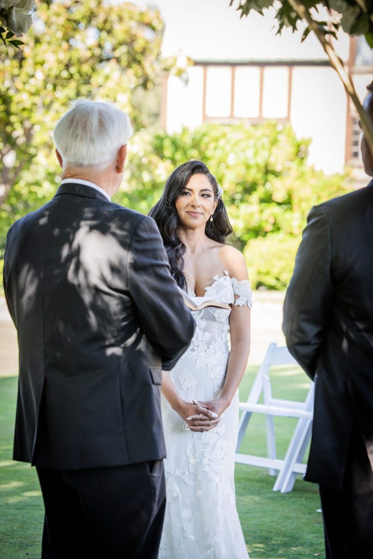 Bride smiling at groom during vows on lawn
