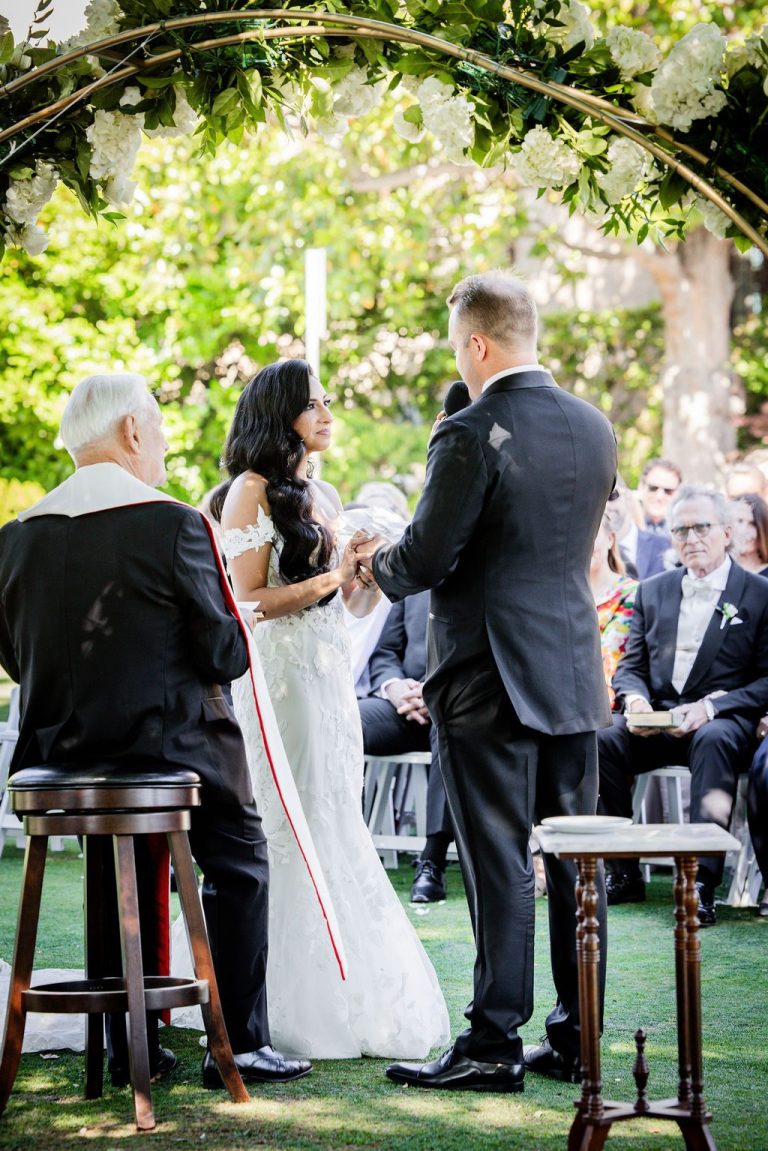Officiant with couple exchanging rings under leafy arch