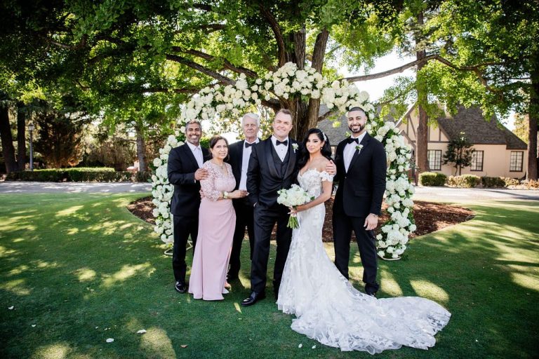 Large family group posed under white floral arch