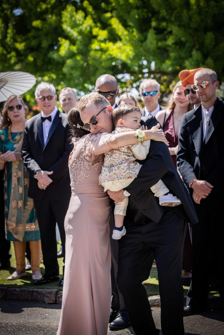 Woman in blush embracing man holding child during greeting